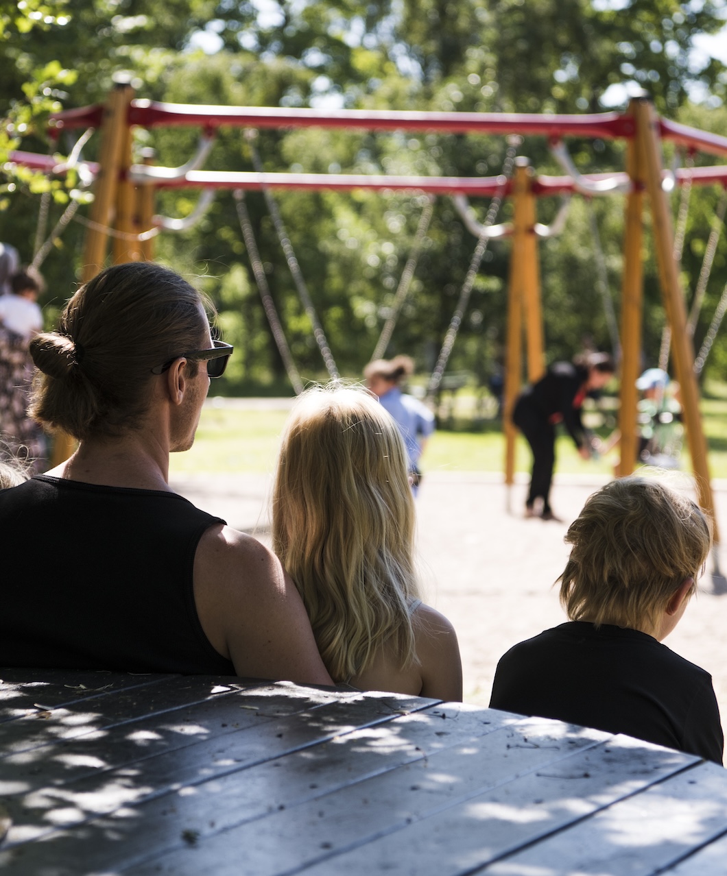 Tre personer sitter och tittar bort mot en lekplats