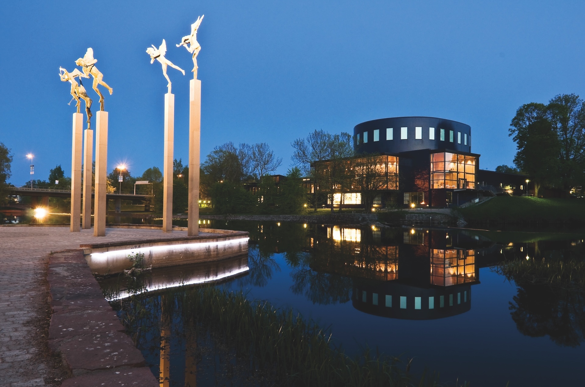 Statyer framför vatten och rund byggnad en kväll