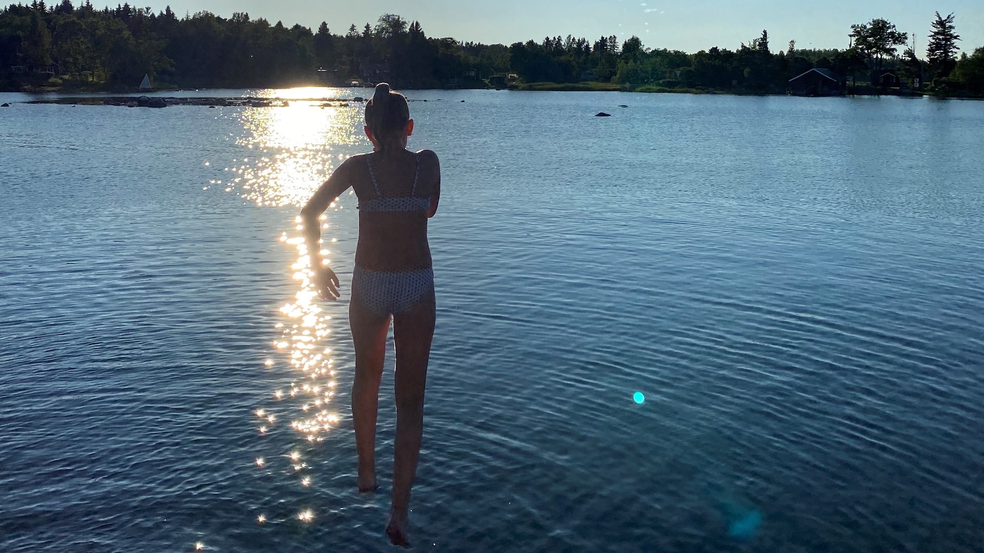 Barn hoppar i vattnet i motljus