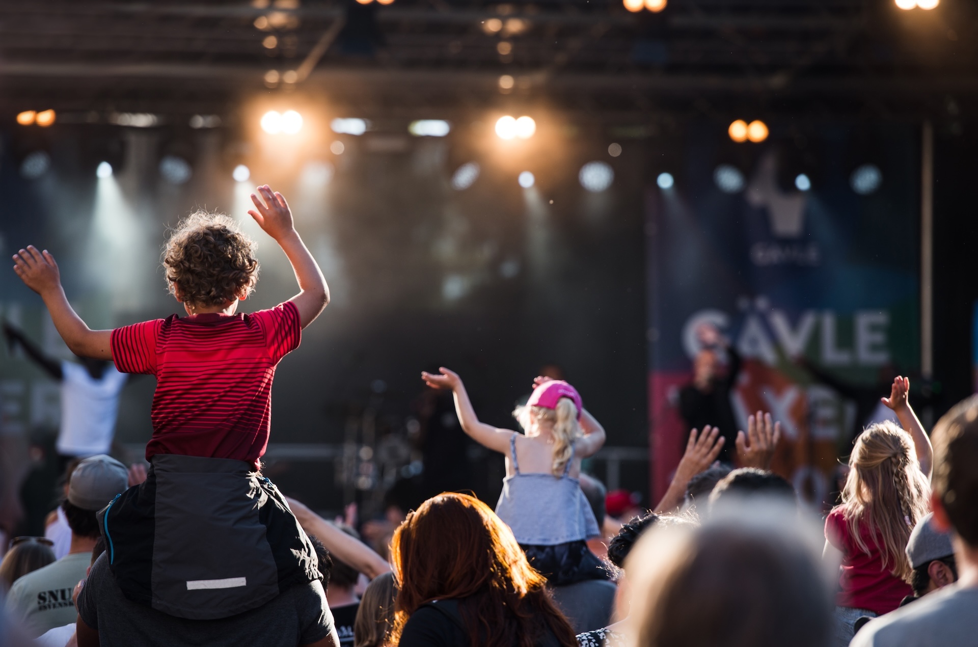 Barn sitter på vuxnas axlar i publik framför scen