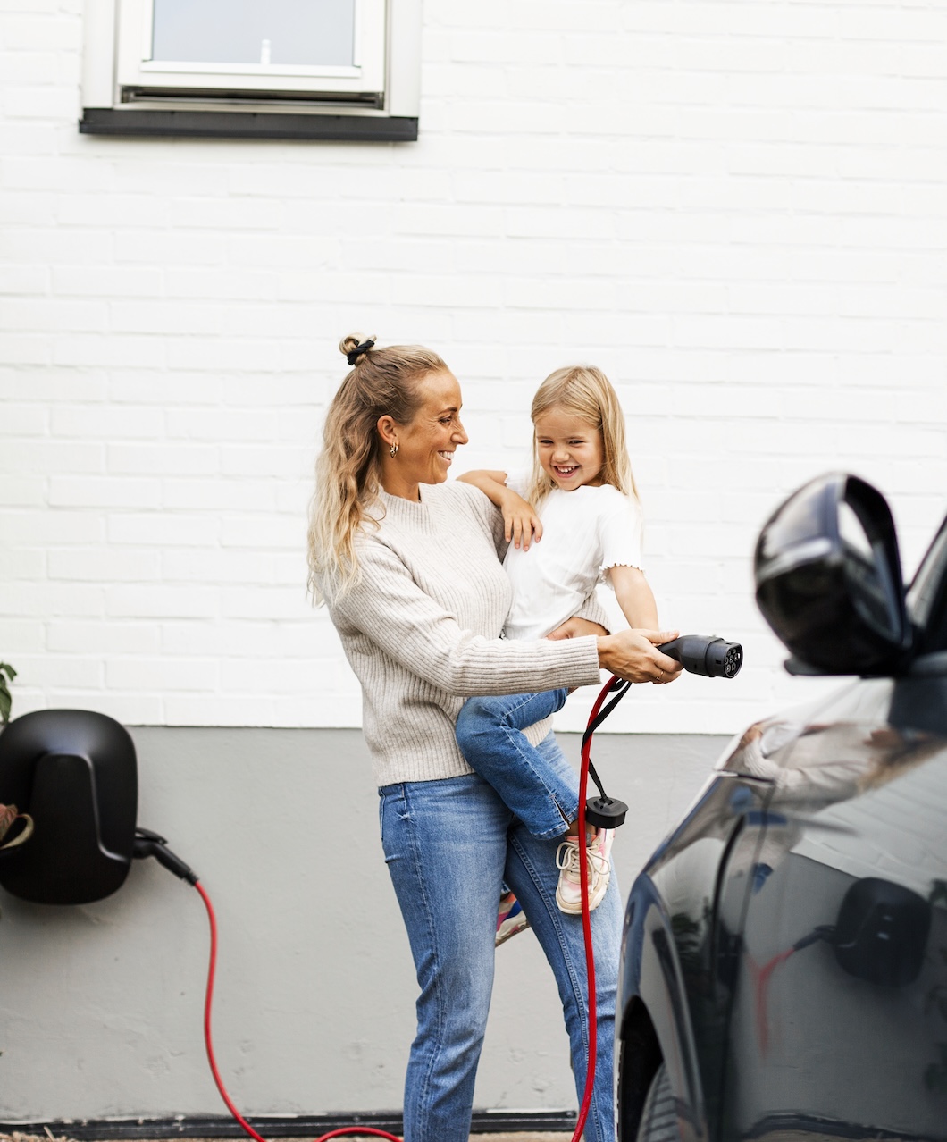 Mamma bär dotter på armen och laddar elbil