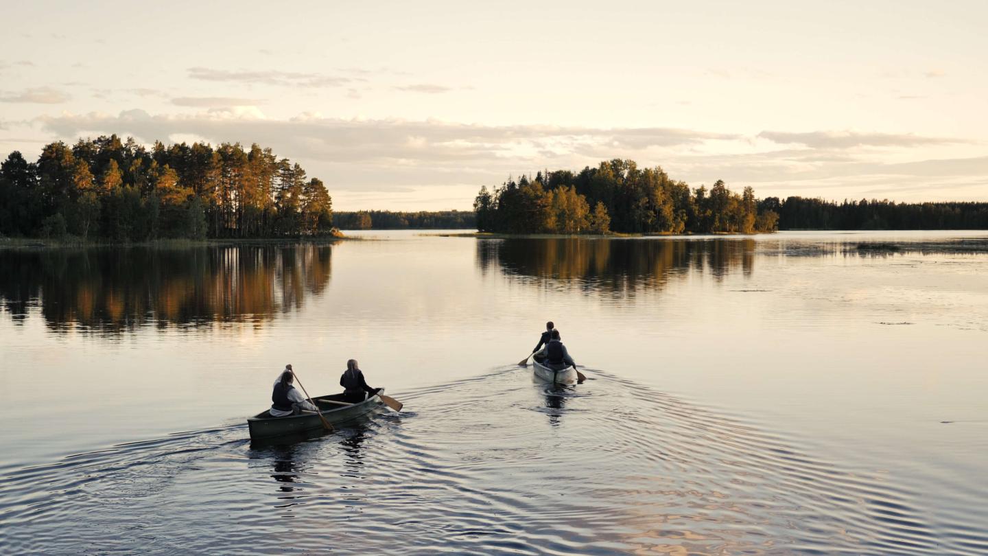 Kanotister i två kanoter glider genom vatten en fin höstkväll