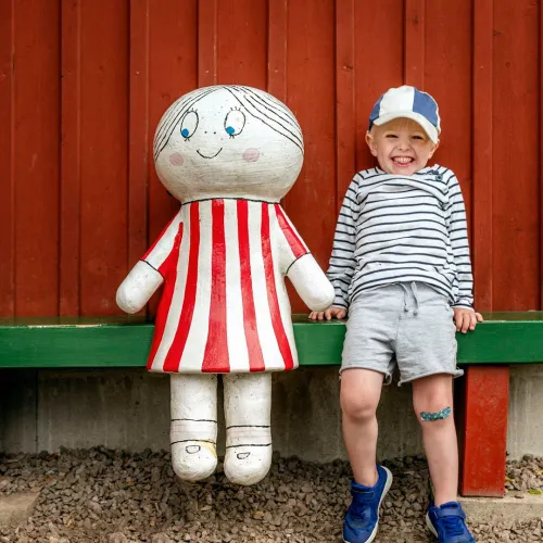 Liten pojke sitter bredvid en sagofigur på en grön bänk mot en röd vägg