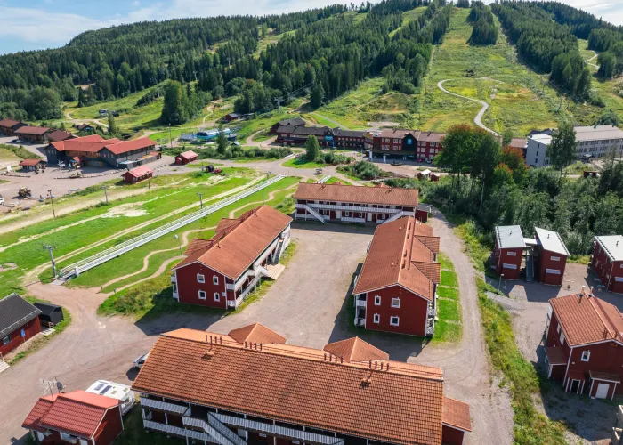 Drönarbild över Kungsberget på sommaren. Hus, stugor, skog och backar syns. Det är en solig dag med gröna områden. 