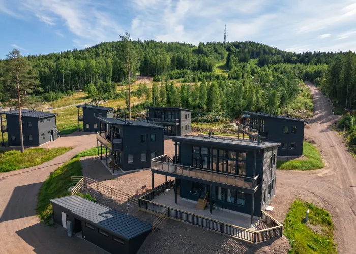 Drönarbild över lägenhetsboendet Panorama på sommaren. Det är en solig dag med gröna områden och skidbacken i bakgrunden. 