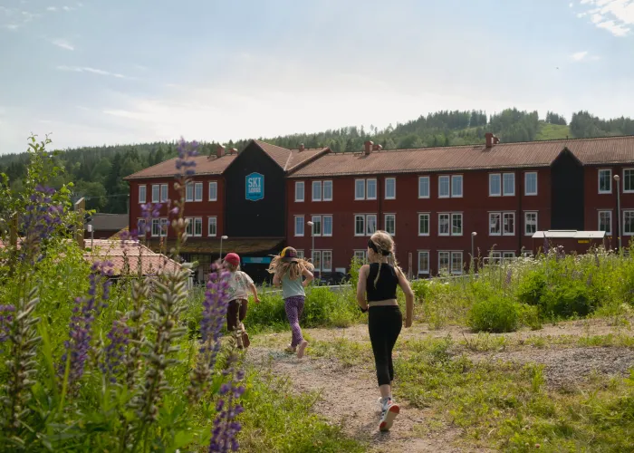 Tre barn springer Äventyrsloppet i en grönskande miljö. I bakgrunden syns Ski Lodge samt Kungsberget.