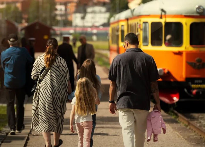 Besökare som går på en perrong mot en gammal orange rälsbuss