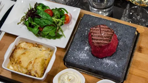 Vackert upplagt med mat på ett bord. En köttbot som är rare, lite sallad och potatisgratäng