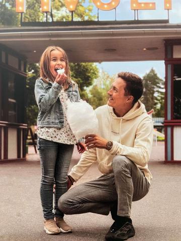 Vuxen person sitter på knä intill ett barn som står och äter glass