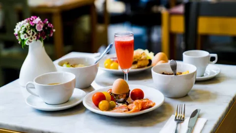 Brunch med kaffe, ägg, frukt och vas med blommor på ett bord med vit duk