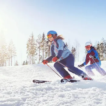 Två skidåkare åker slalom nerför en skidbacke en fin vinterdag