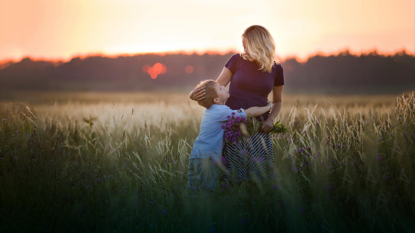 Barn kramar mamma på en äng en härlig sommarkväll